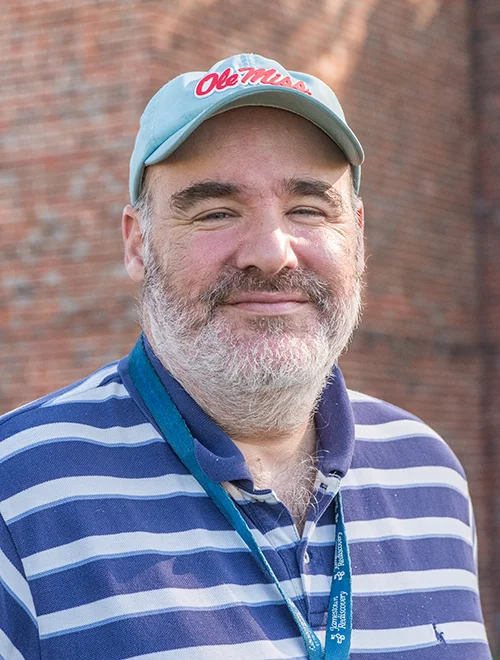 photo of person standing outdoors in baseball cap with lanyard around neck