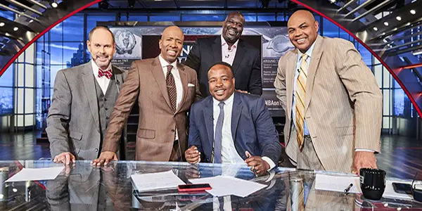 group of people standing behind one person deated at a desk in a TV broadcast set