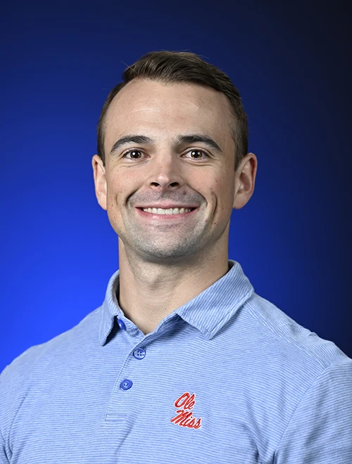 Formal portrait of Colter Clayton, smiling, blue background.