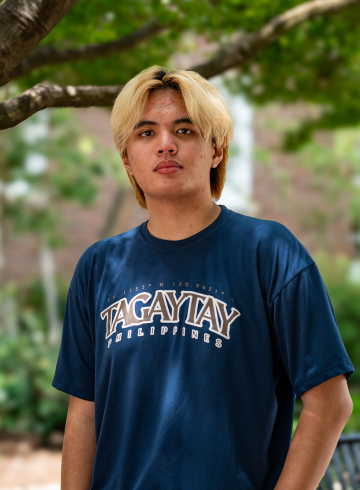 Matt Oliver Natanauan on campus, standing underneath one of the shade trees on the western side of the library