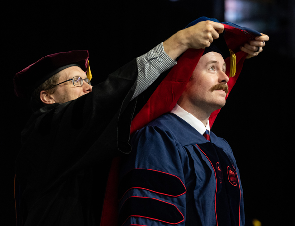 student at graduation ceremony receiving their master's hood