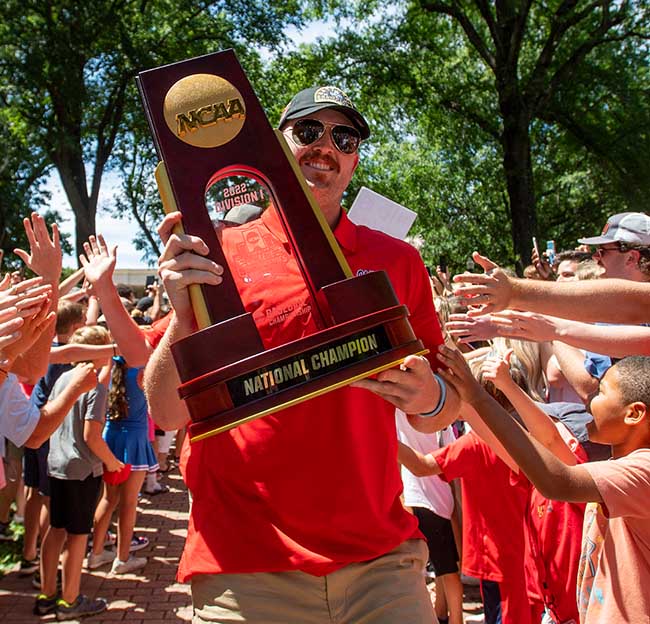 Tim Elko carries the NCAA Division 1 National Championship Baseball Trophy through the Grove down the Walk of Champions.