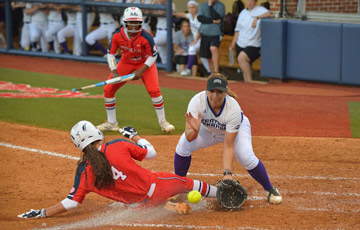Ole Miss softball player sliding into a base. Opposing player is squatting to try to catch the ball in the air.