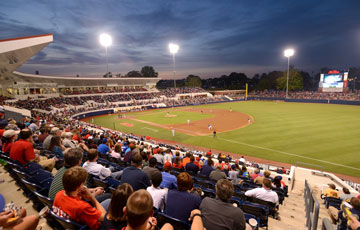 Night baseball game at Swayze Field. Spectators in foreground, green baseball diamond in middle ground, and night sky lit up with stadium lights in background.