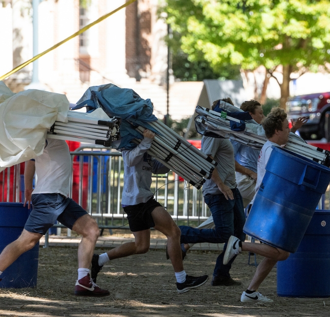 Students run with tents on their shoulders to secure their tailgate spot in the Grove the Friday before game day.