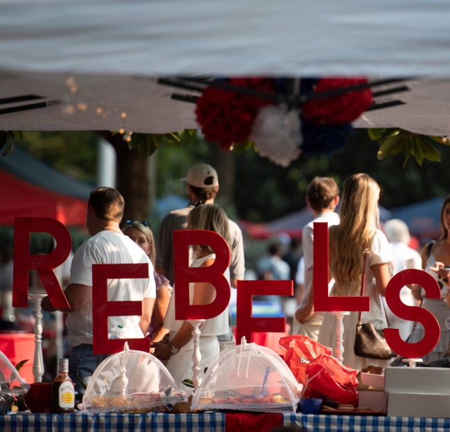 A sign that says "Rebels" on a table full of tailgating food