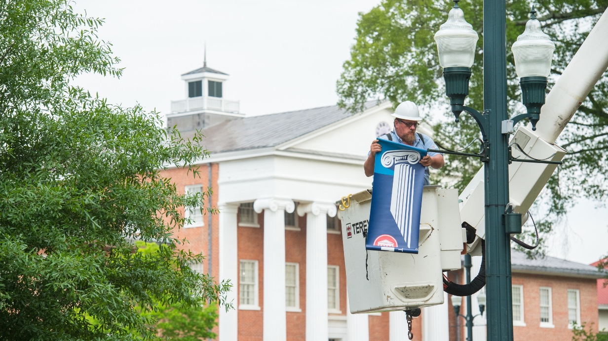 Facilities staff hanging sign on campus