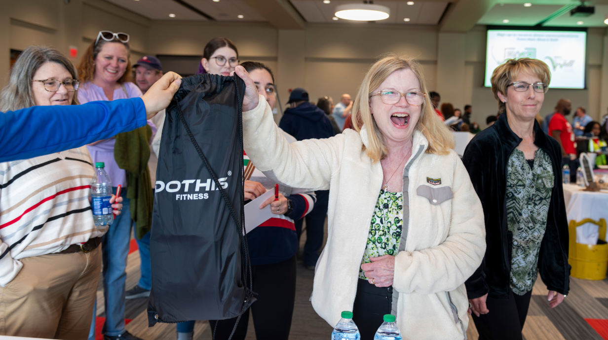 Photo of faculty member smiling as she interacts with other staff members at a university event. 