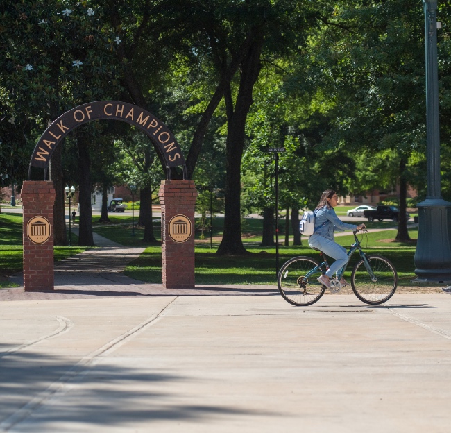 Student rides on a bike past the entrance to the Walk of Champions.