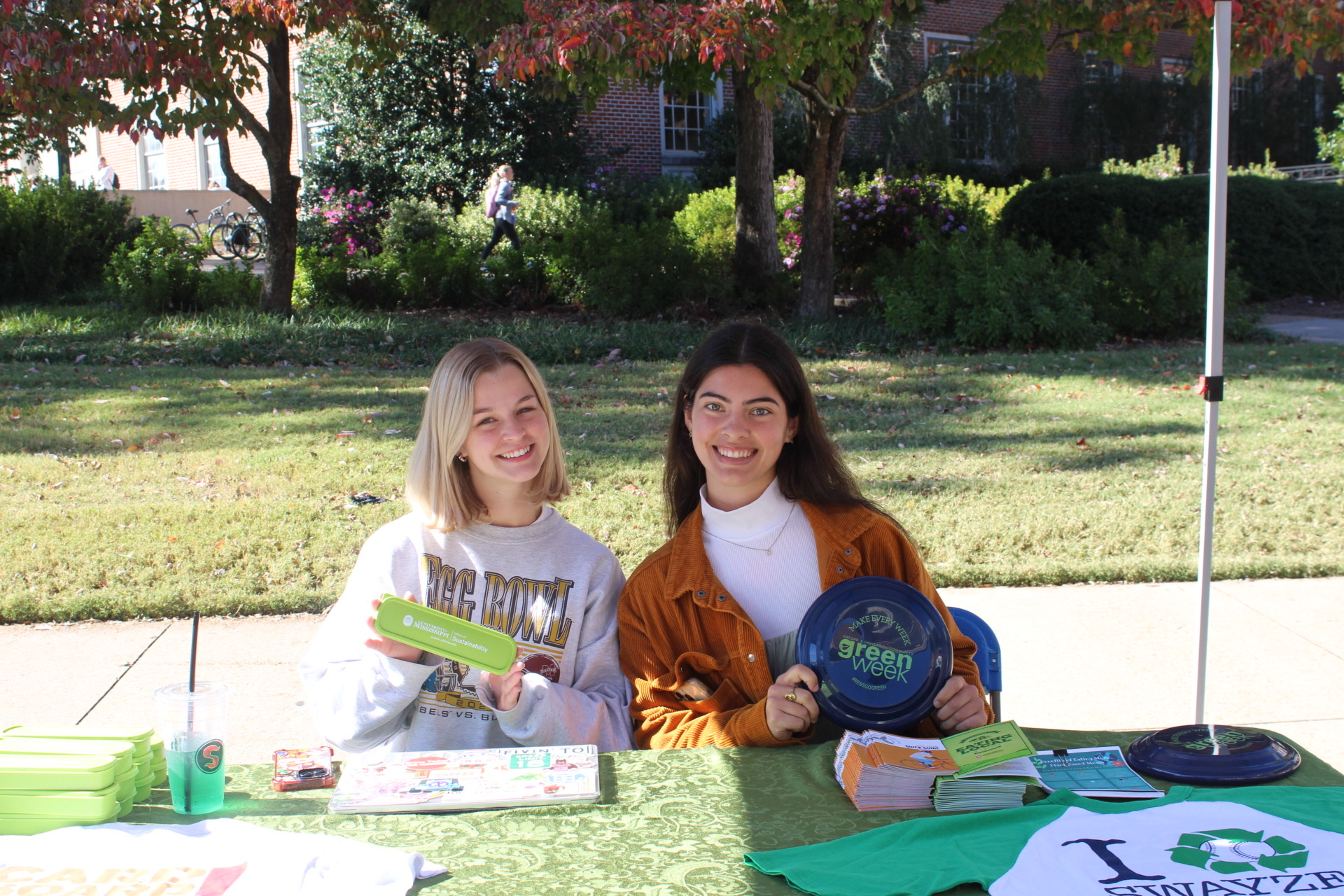 Two smiling Office of Sustainability interns tabling on campus distributing flyers and swag.