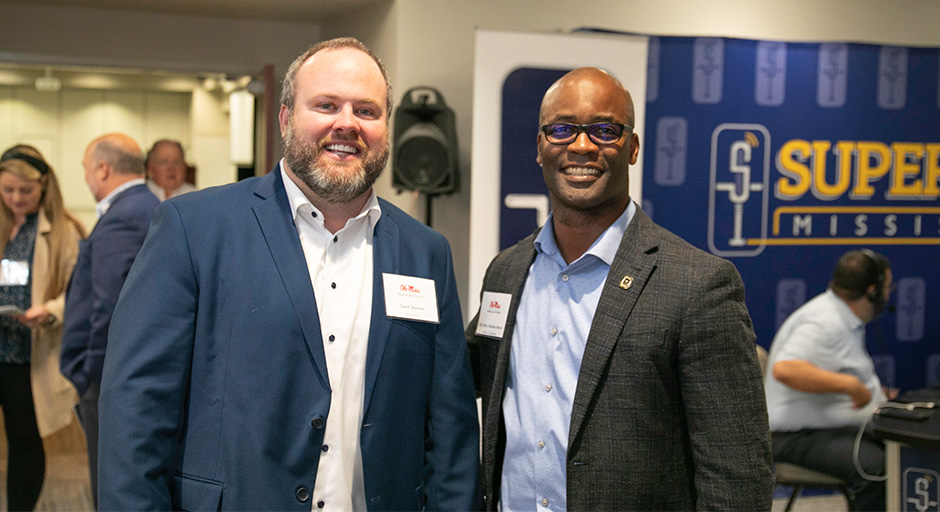 Two men posing for a photo in from of the Super Talk banner during the symposium.