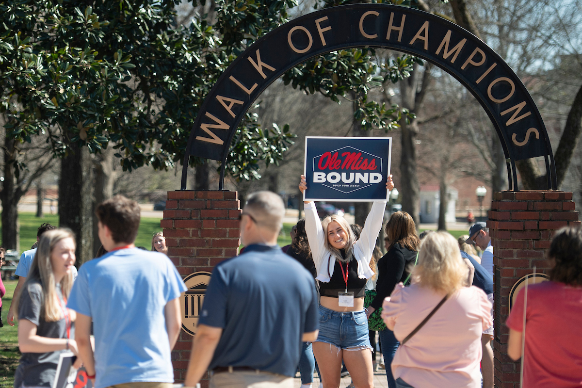 Student holding sign in front of the Walk of Champions on campus. The sign reads Ole Miss Bound. 