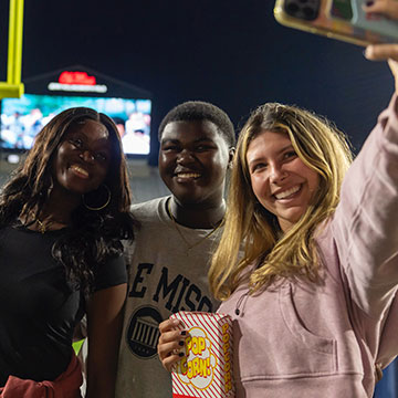 Students pose for a photo at an Ole Miss football game in front of the field