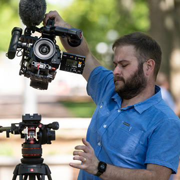 A man on campus puts a camera on a tripod