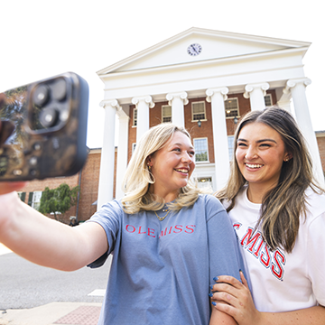 Two students taking a selfie in front of the University of Mississippi Lyceum.