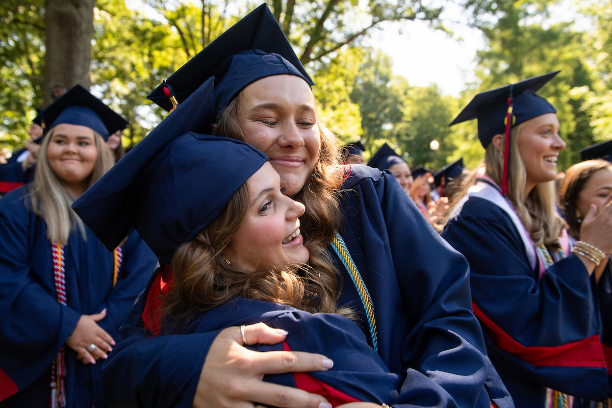 two students wearing graduation caps and gowns hugging