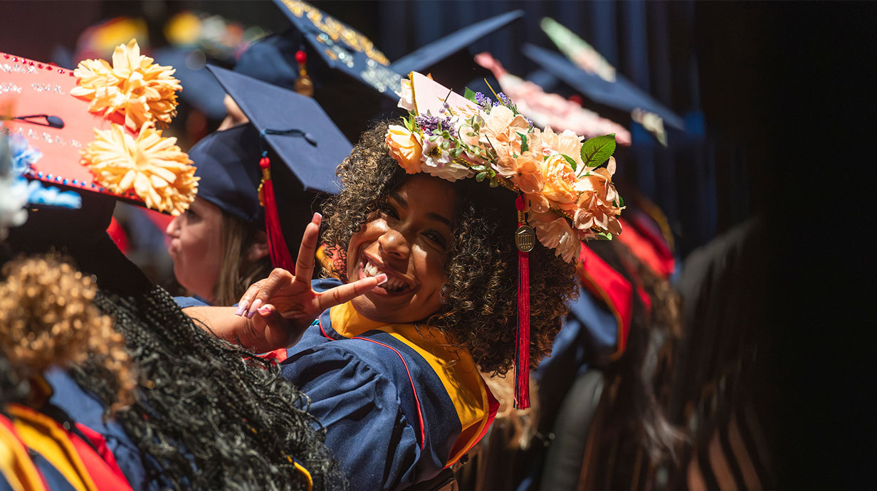 A 2024 Ole Miss graduate smiles and makes a peace sign during commencement.