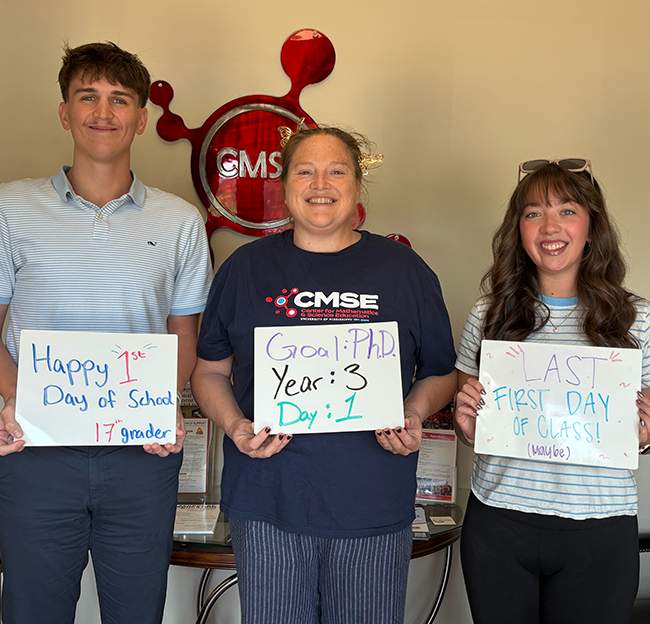 One man and two women stand side by side smiling at the camera while holding mini white board signs.