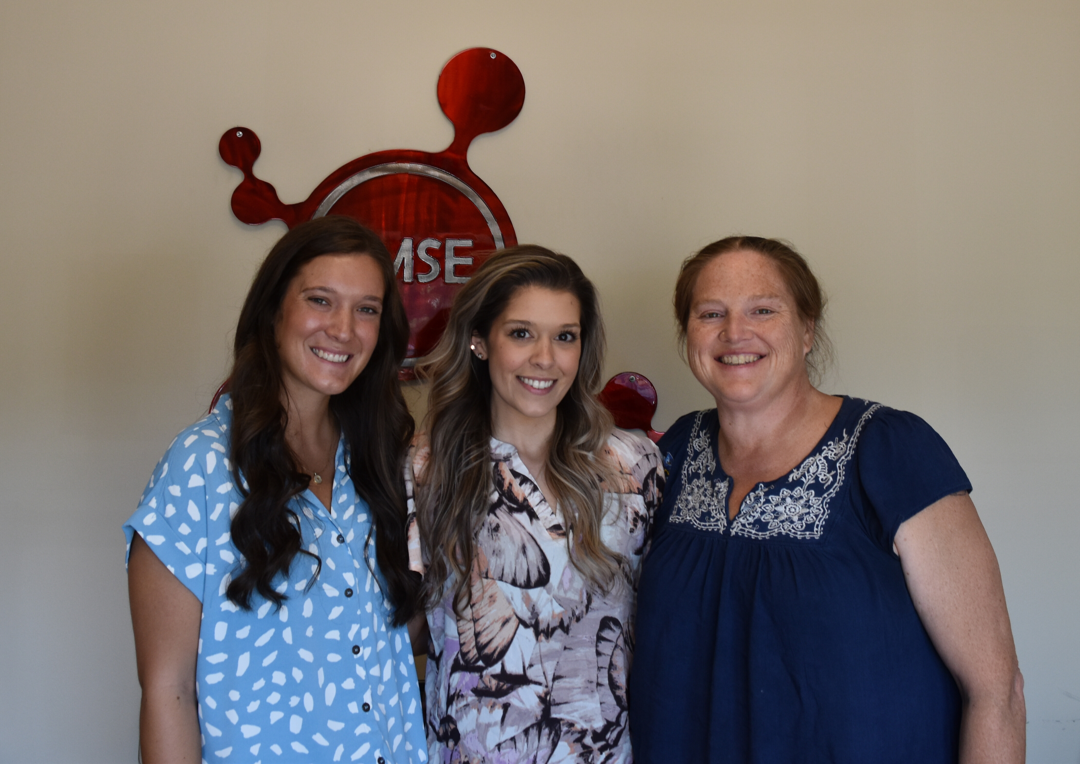 Three students pose in front of the CMSE logo.