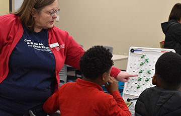 Female teacher points to parts of a turing tumble activity with two students watching.