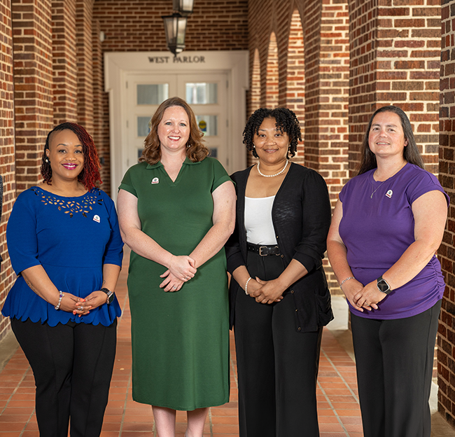 Four women stand smiling in a hallway with brick walls.