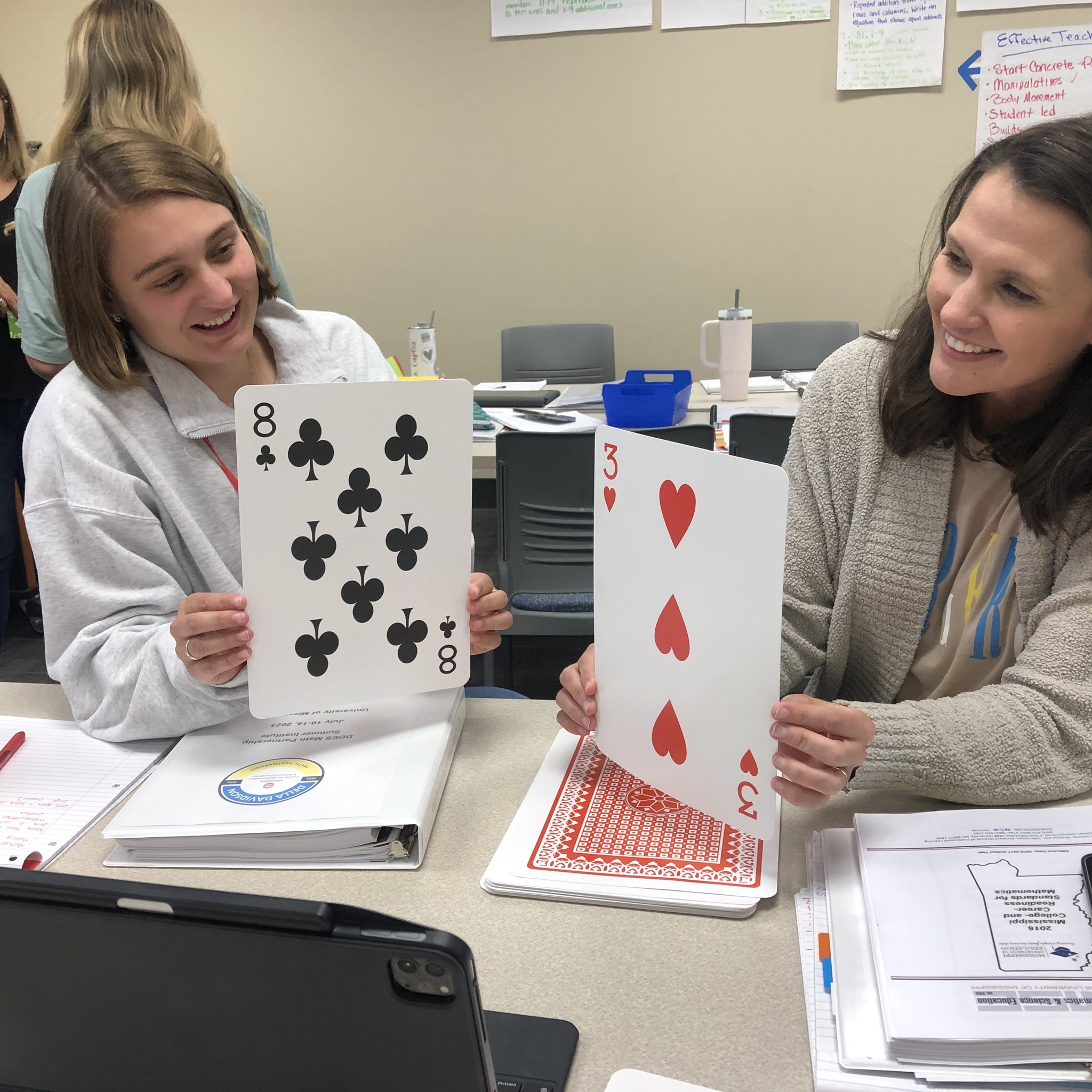 Two teacher hold up large playing cards during a learning activity.