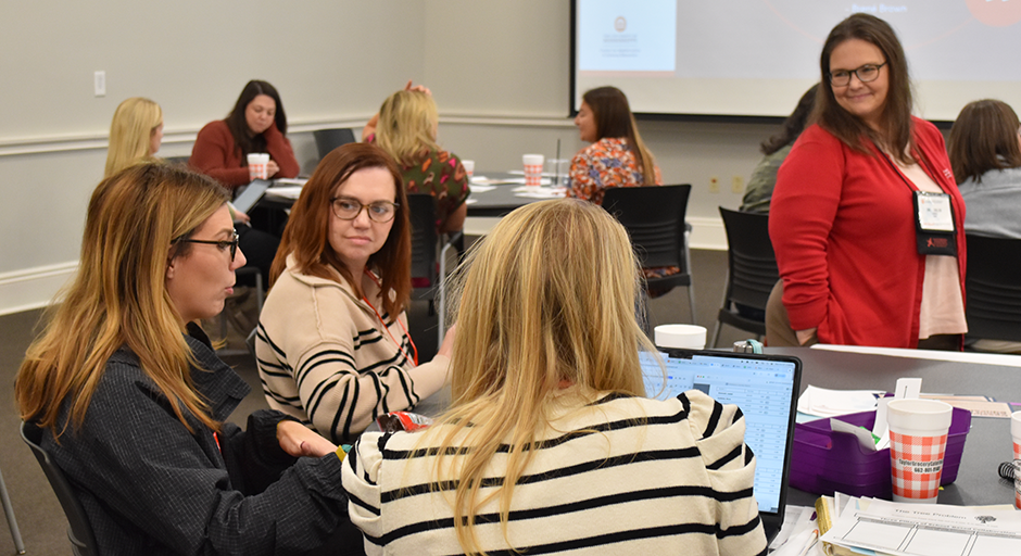 A group of math teaches engages in discussion around a table in a conference room.