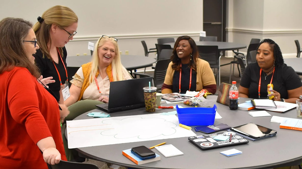 Five women sit around a table, engaged in a lively math discussion.