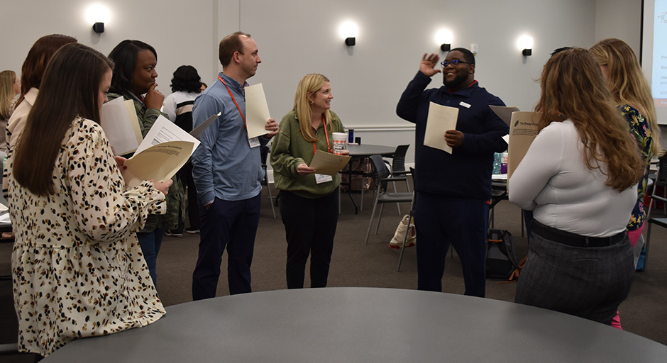 A group of math educator stand in a circle, holding papers and engaging in animated conversation.