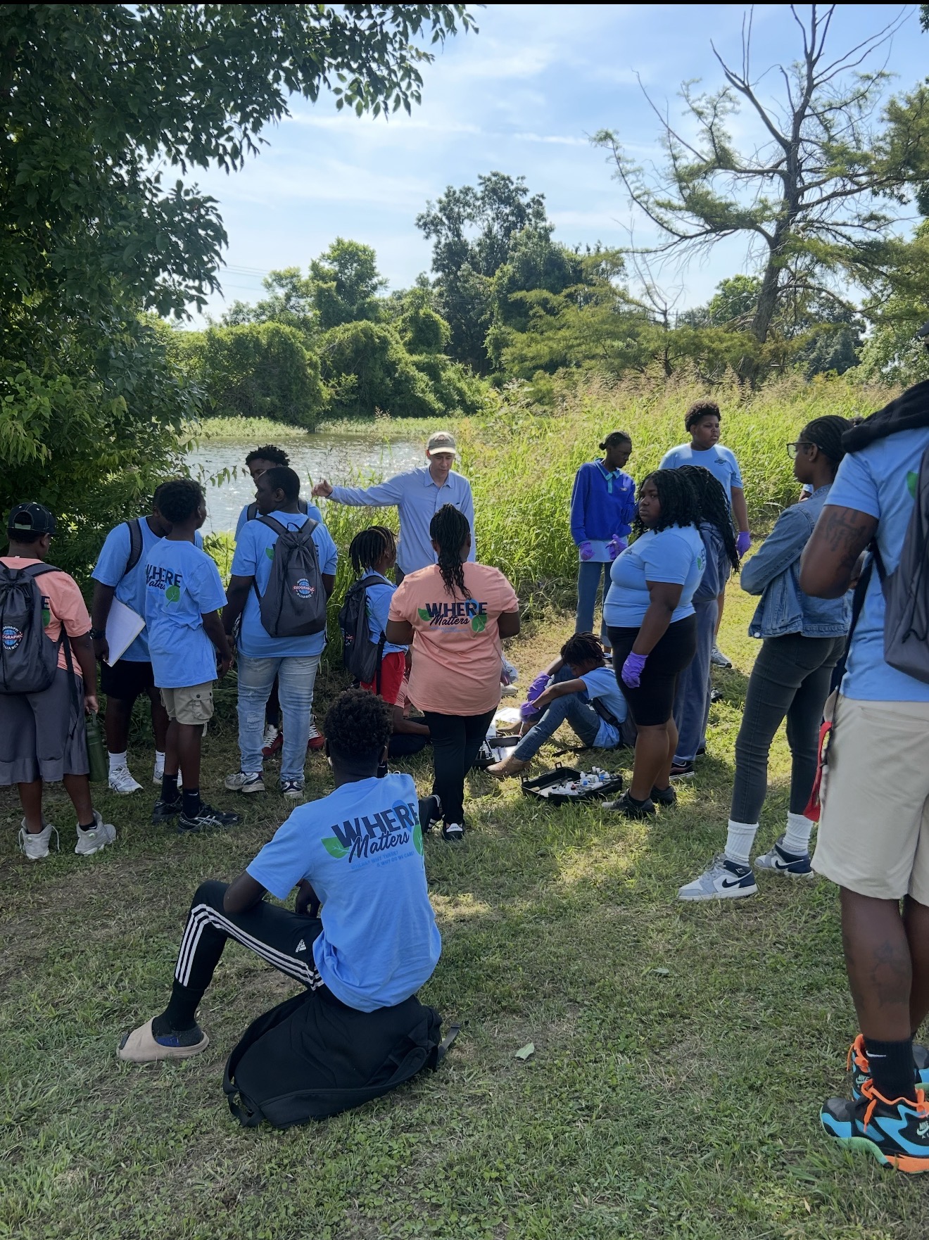 An instructor leads a discussion outdoors as a group of students closely observe and listen.