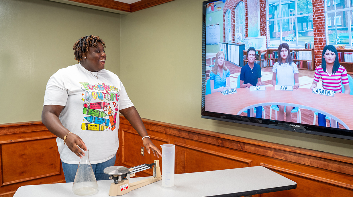 Teacher demonstrates a science experiment with a scale, beaker, and graduated cylinder for a virtual classroom of student avatars named Savannah, Dev, Ava, and Jasmine displayed on a wall-mounted screen.