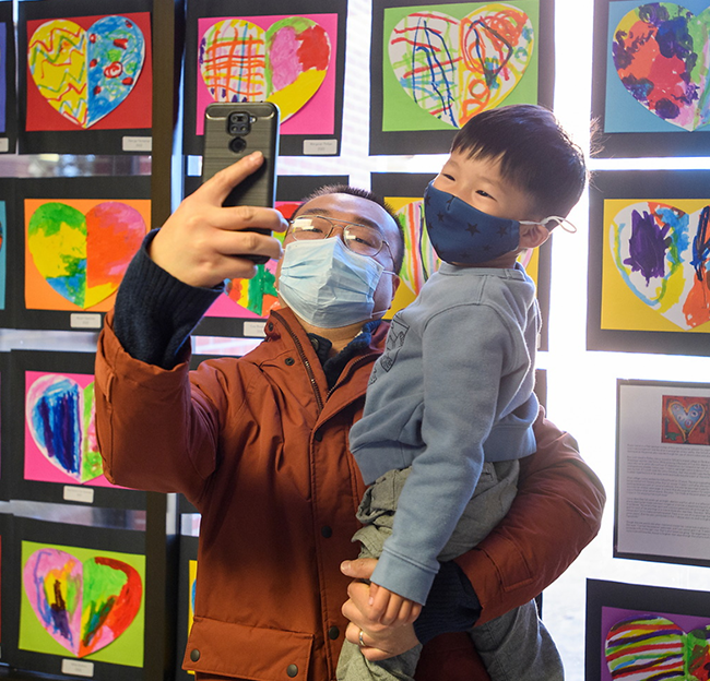 a father and his son taking a photo in front of children's art work