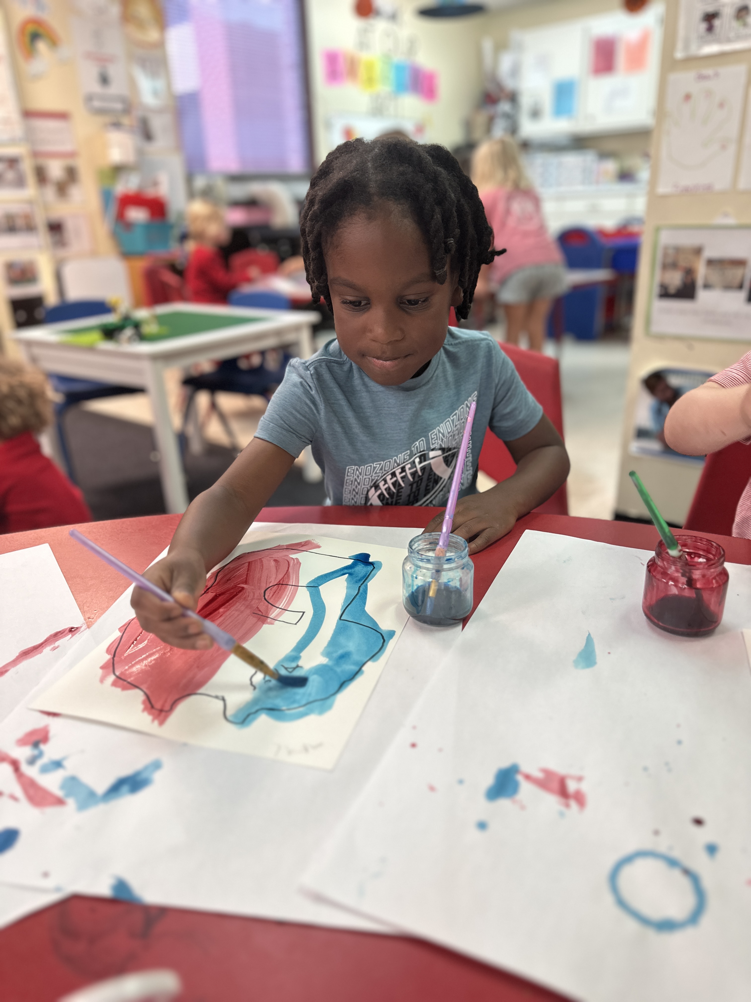 A young student is painting using red and blue water colors.
