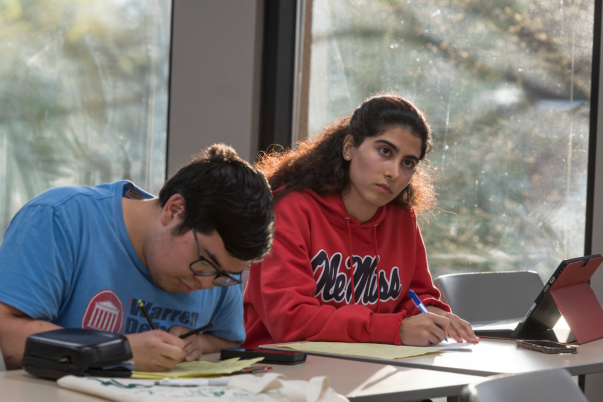 Two students take notes in a classroom.