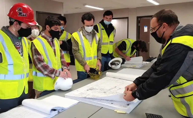 A group of students in high-vis vests view construction plans