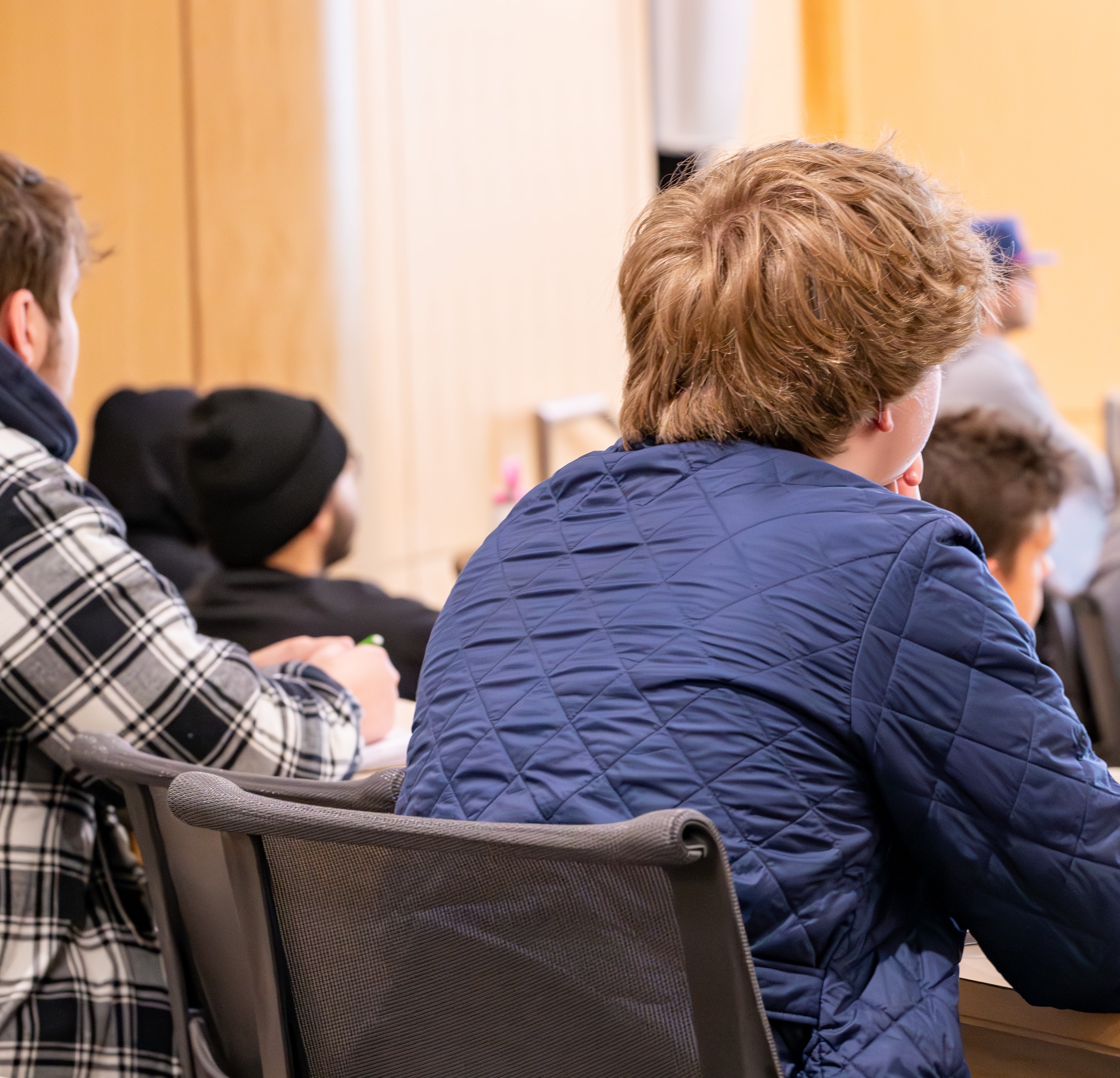 A shot from behind a student shows them focusing their attention to the front of the classroom