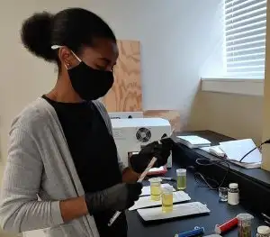 A student stands in a lab holding an instrument to test for lead in water.