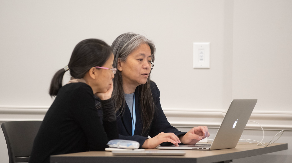 Two computer science instructors sit at a table looking intently at the screen of a laptop in front of them