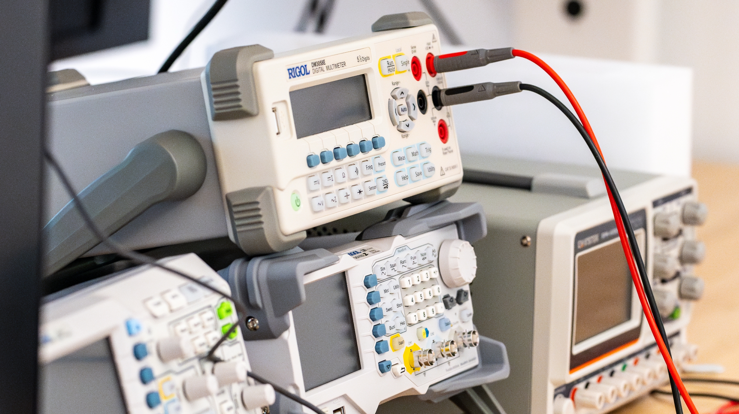 A stack of digital multi-meters sitting on a table. A red and black wire and plugged into one multi-meter.