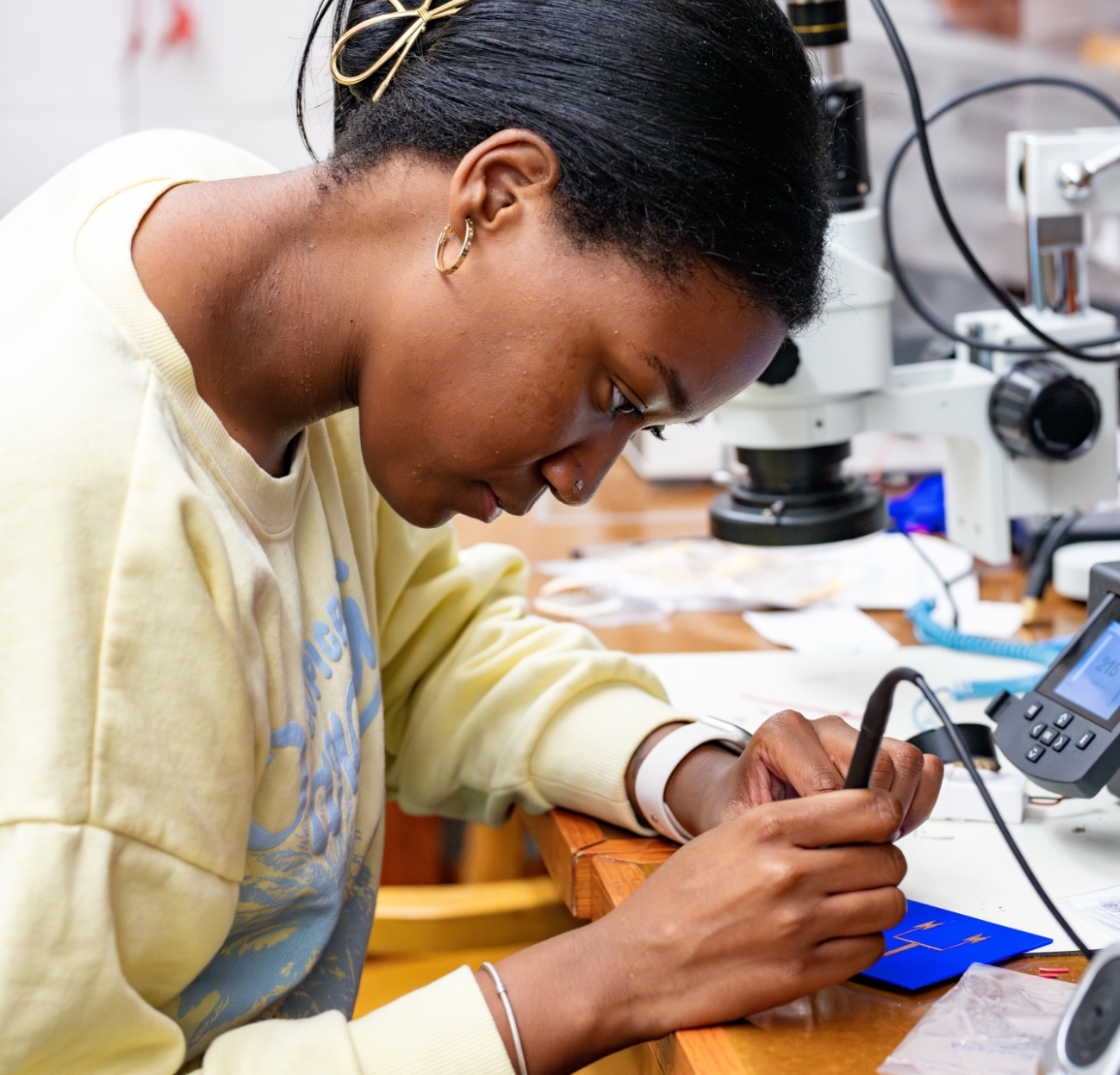 A student sits at a desk using a multi-meter in an electrical engineering lab.