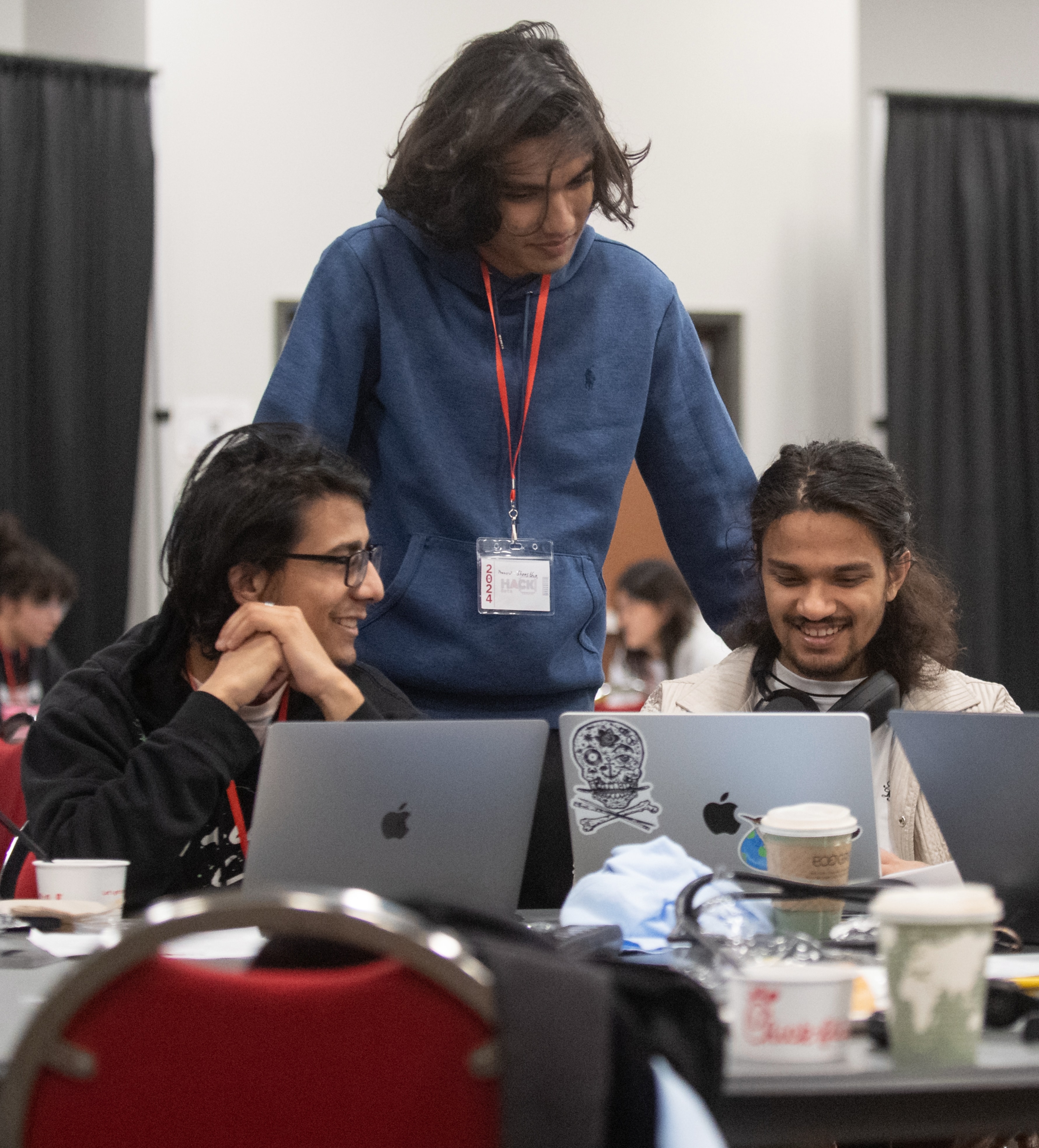 A group of students smile and huddle around their computers during a hack-a-thon.