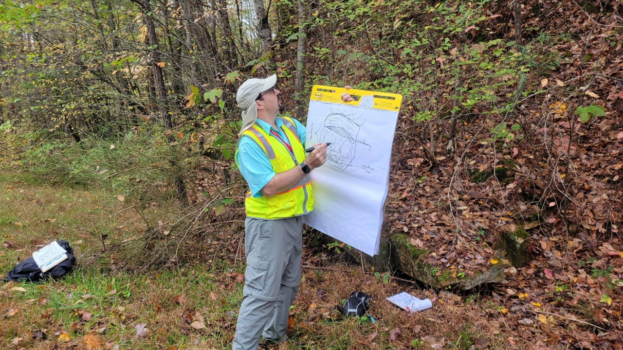 A geology instructor draws a diagram on a large white canvas outdoors