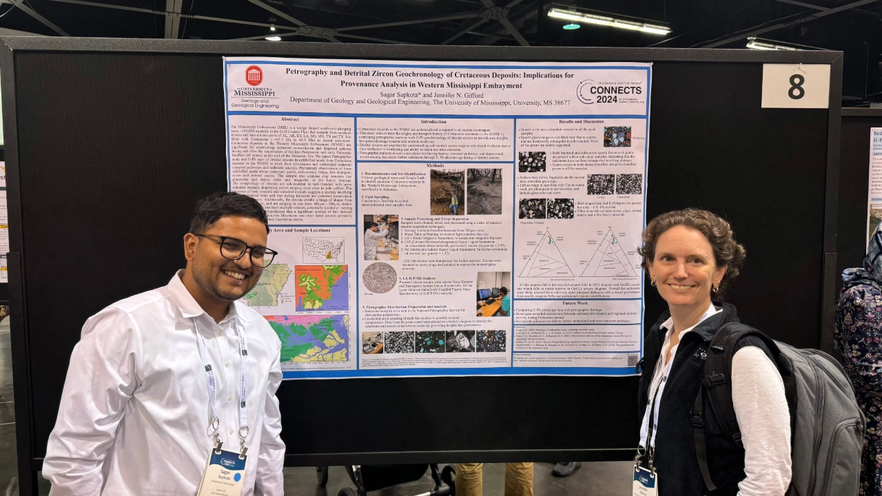 Two researchers standing in front of an infographic explaining the details of their geology project.