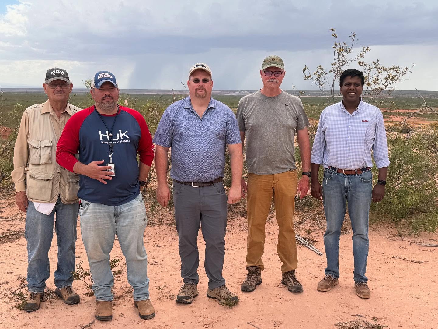 A group of geology researchers stand outdoors at a research location.