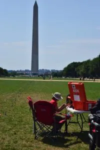 Person seated in a red camping chair with geology tools near the Washington Monument on a sunny day.