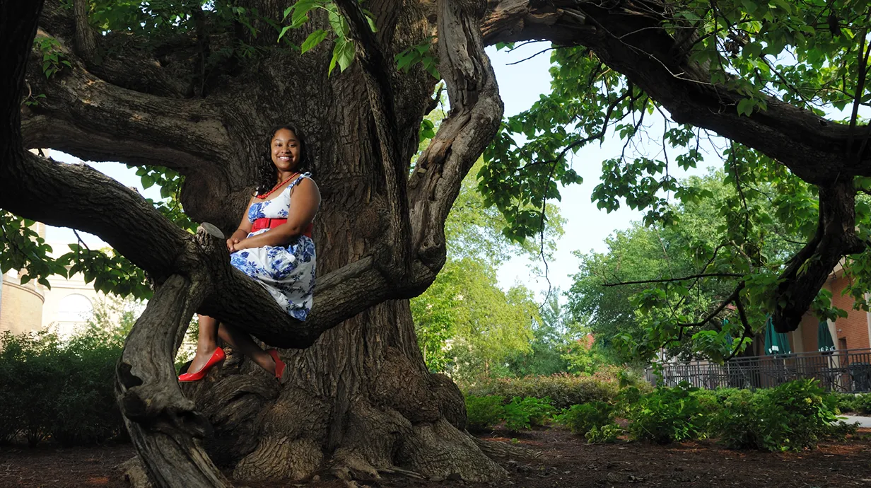 An Ole Miss student poses for a photo while sitting on a branch of a tree outside of Bryant Hall.