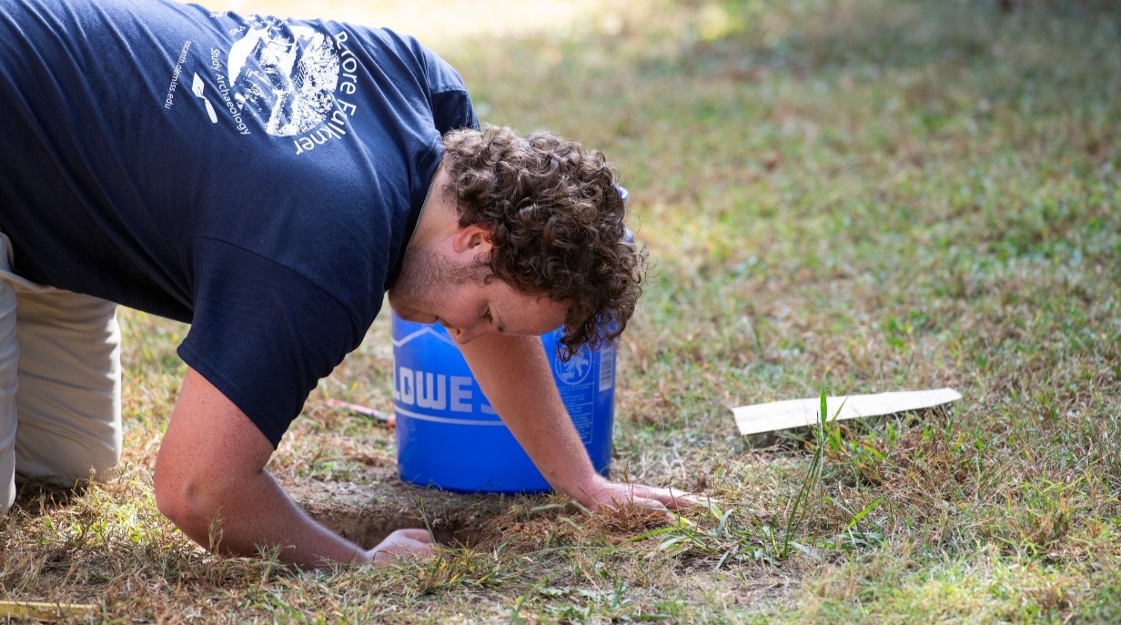 student kneeling on the ground and peering into a hole in the ground