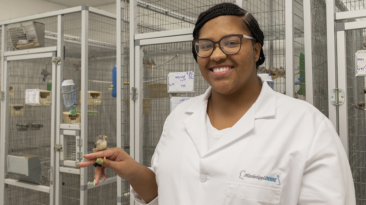 female student smiling and looking at the camera while holding a bird on her finger.