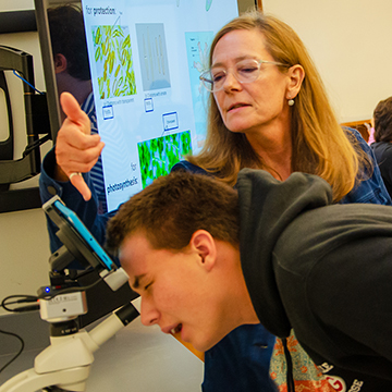 professor pointing something out to a student on a microscope