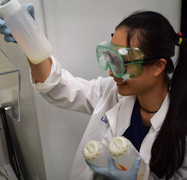 female high school student wearing safety goggles while looking at samples in a container